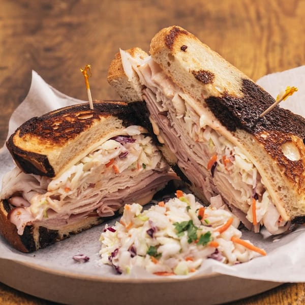 A grilled sandwich with turkey, coleslaw, and cheese, cut in half, served with a side of coleslaw.