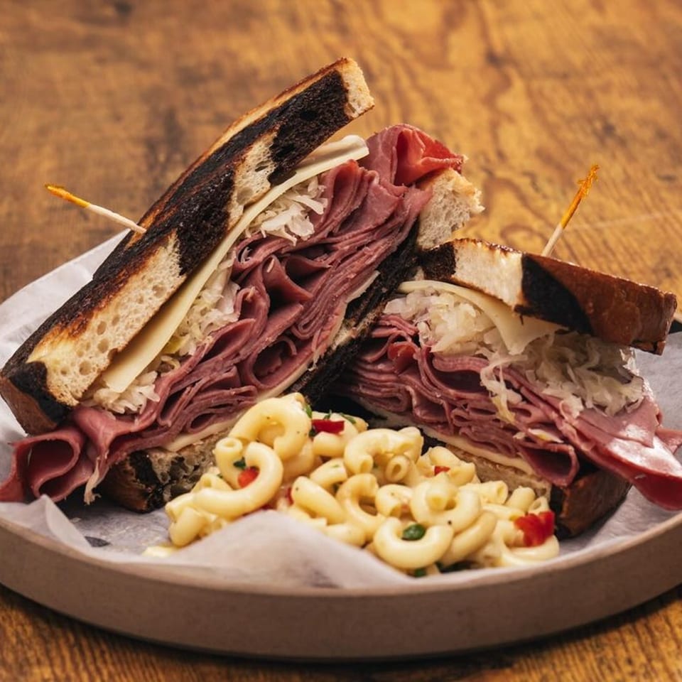 A Hot Tomatoes Italian deli sandwich with pastrami, Swiss, sauerkraut, and a side of macaroni salad.