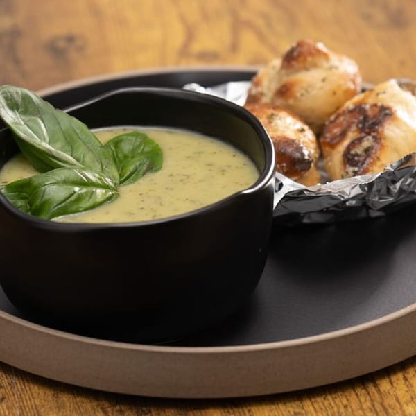Creamy green soup with basil leaves in a black bowl, served with garlic knots.