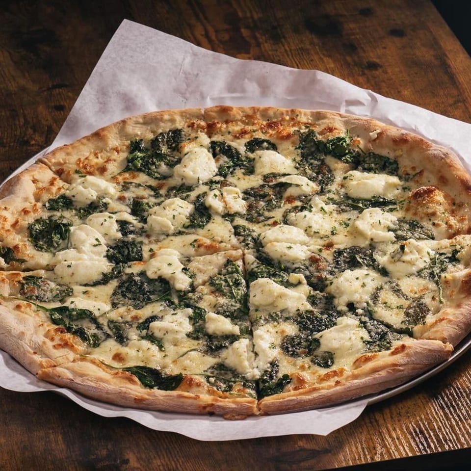 Hot Tomatoes' white pizza with spinach and ricotta cheese on a wooden table.