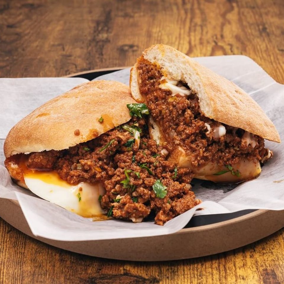 A Hot Tomatoes Italian meatball sub, cut in half, overflowing with rich sauce and melted cheese.