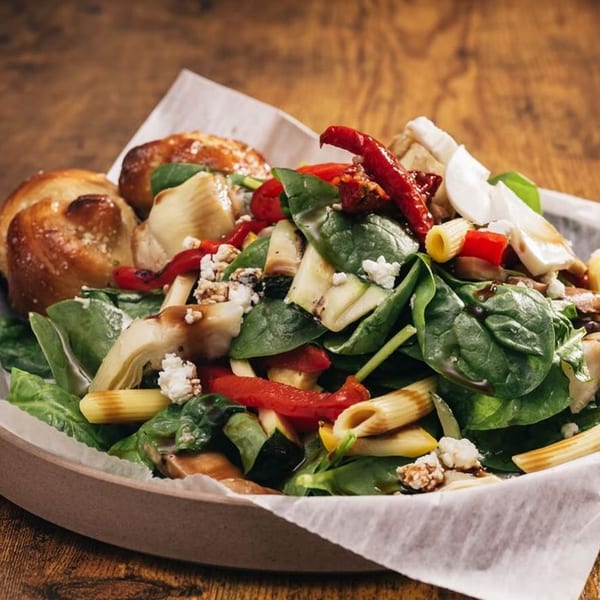 Italian pasta salad with spinach, red peppers, artichokes, feta, and two bread knots.